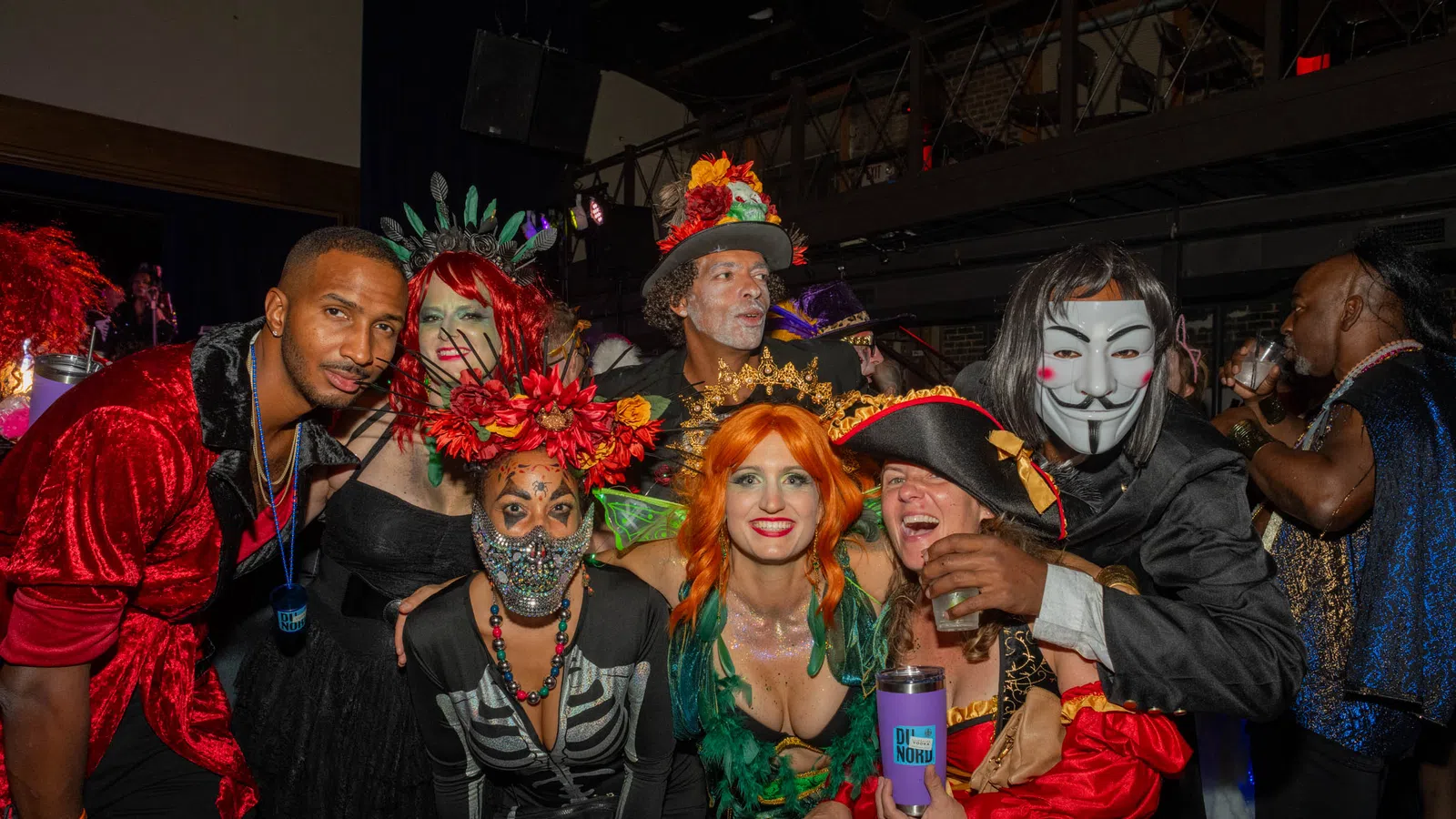 Group of adults in colorful and creative costumes posing indoors at a lively Halloween or costume party.