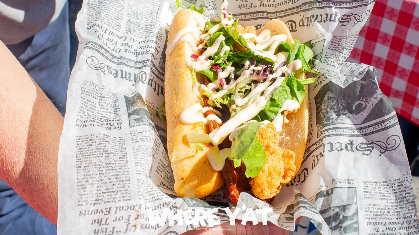 Fresh fried fish sandwich with lettuce and sauce served in newspaper-style wrapping held by a person.