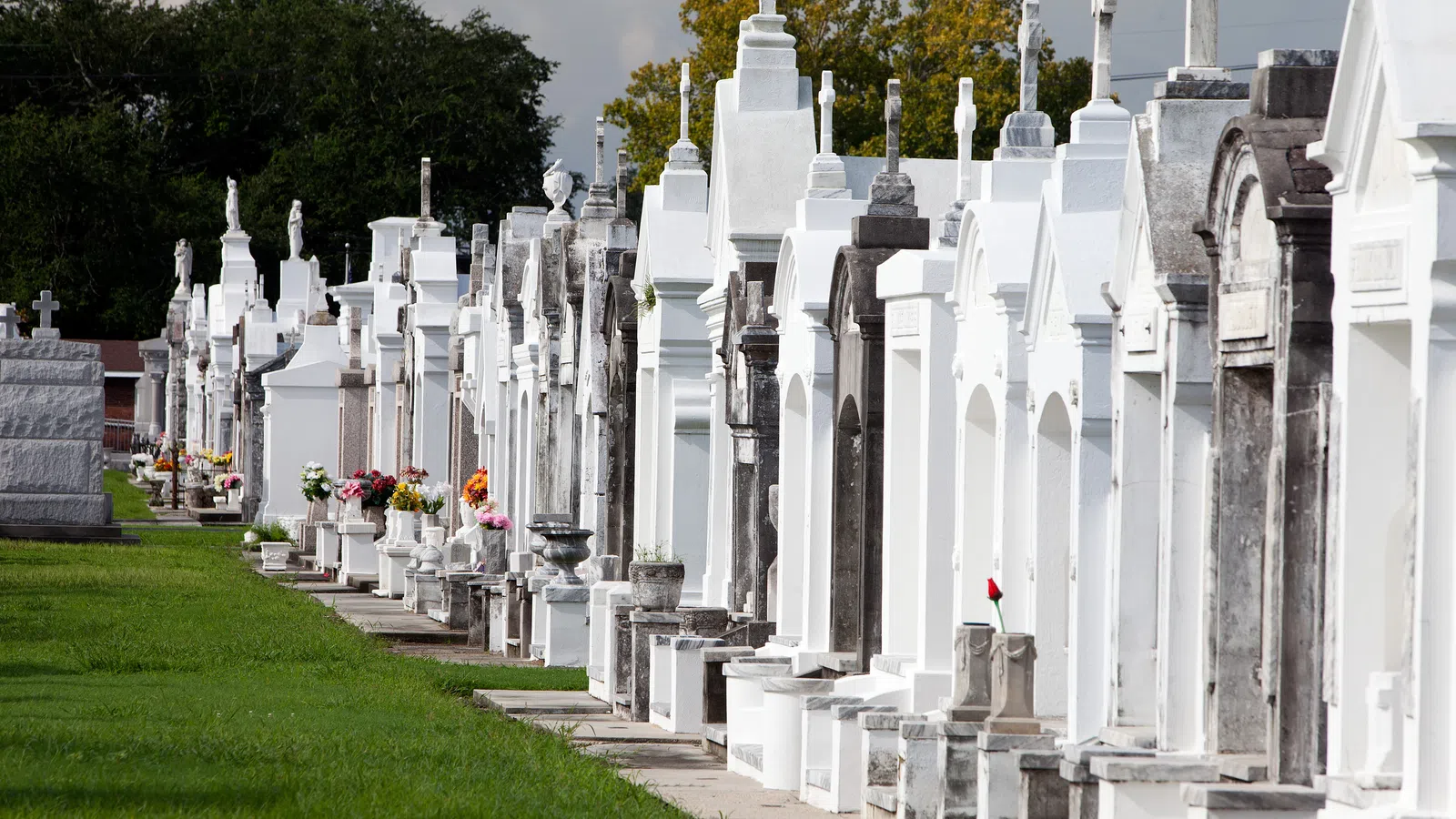 Row of white and gray above-ground tombs with flowers in a cemetery on a sunny day.