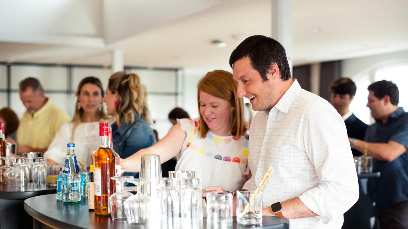 People enjoying drinks and socializing around a modern bar counter with bottles and glasses.