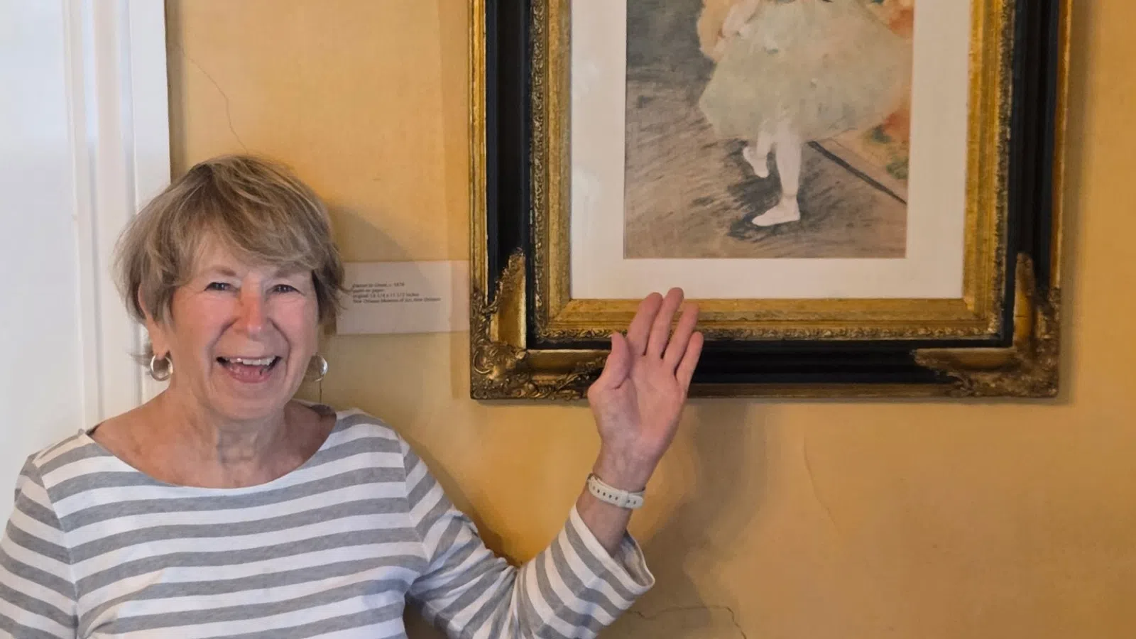 Smiling elderly woman pointing at framed impressionist painting of ballerina in museum setting