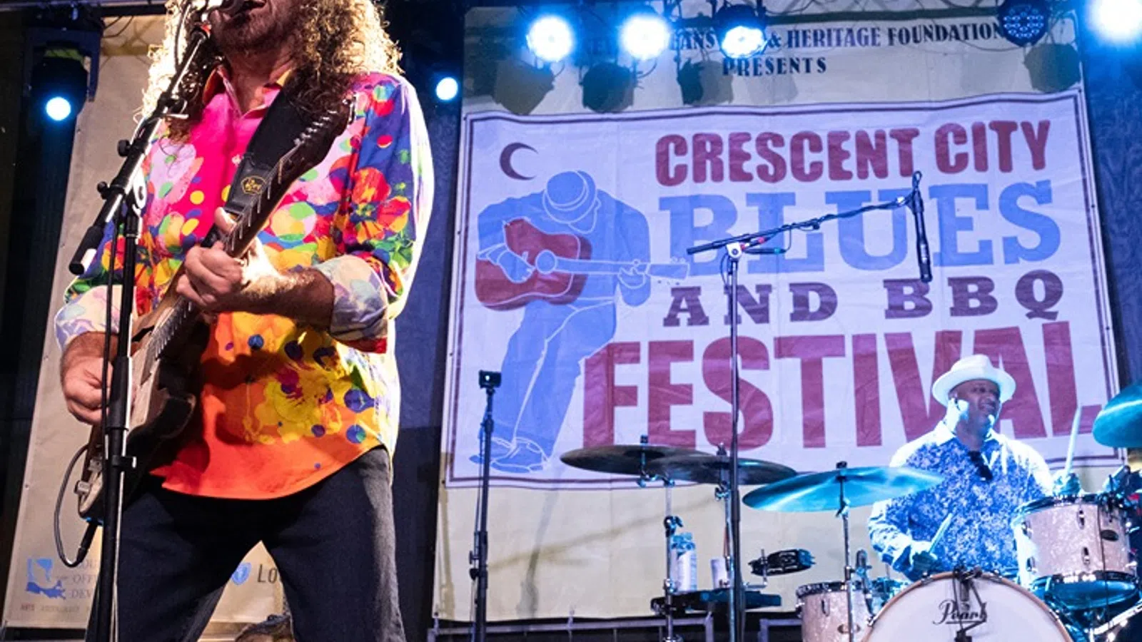 Singer with colorful shirt plays guitar and vocalist performs at Crescent City Blues and BBQ Festival concert.