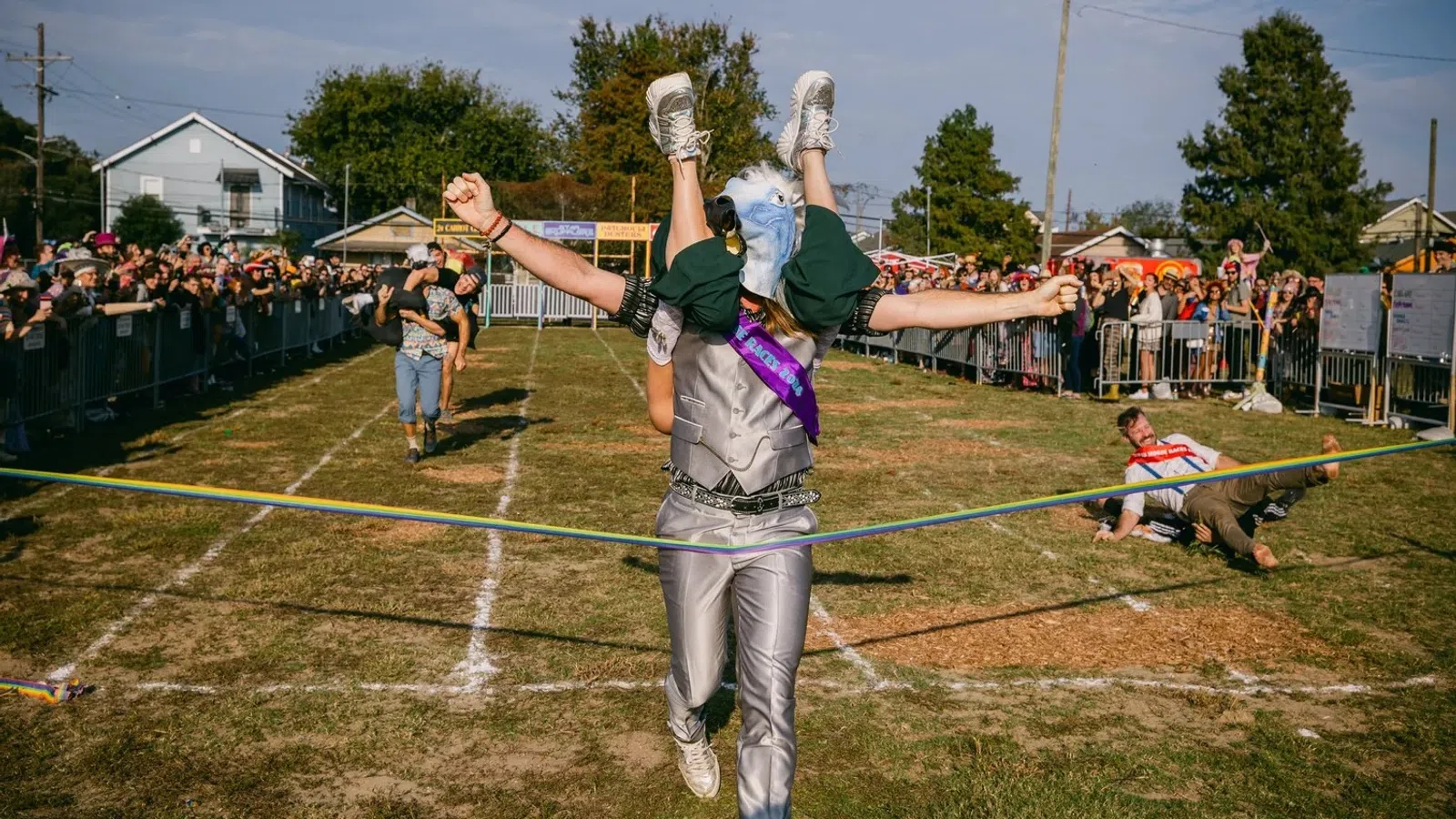 Person in eagle costume winning a race while carrying another runner across the finish line at outdoor event.