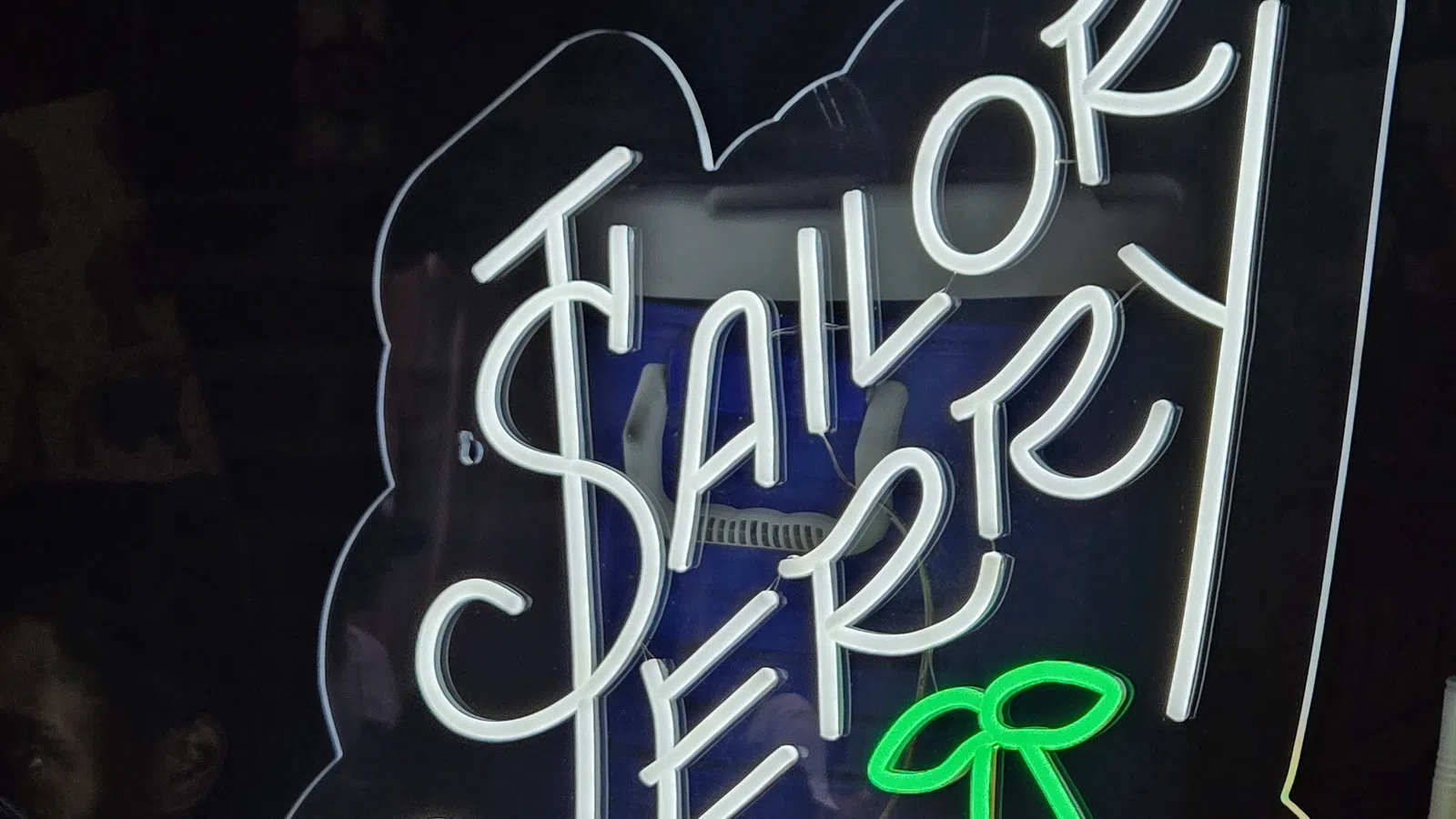 Neon sign displaying the words Sailor Jerry with bright white and red cherry graphics on a dark background.