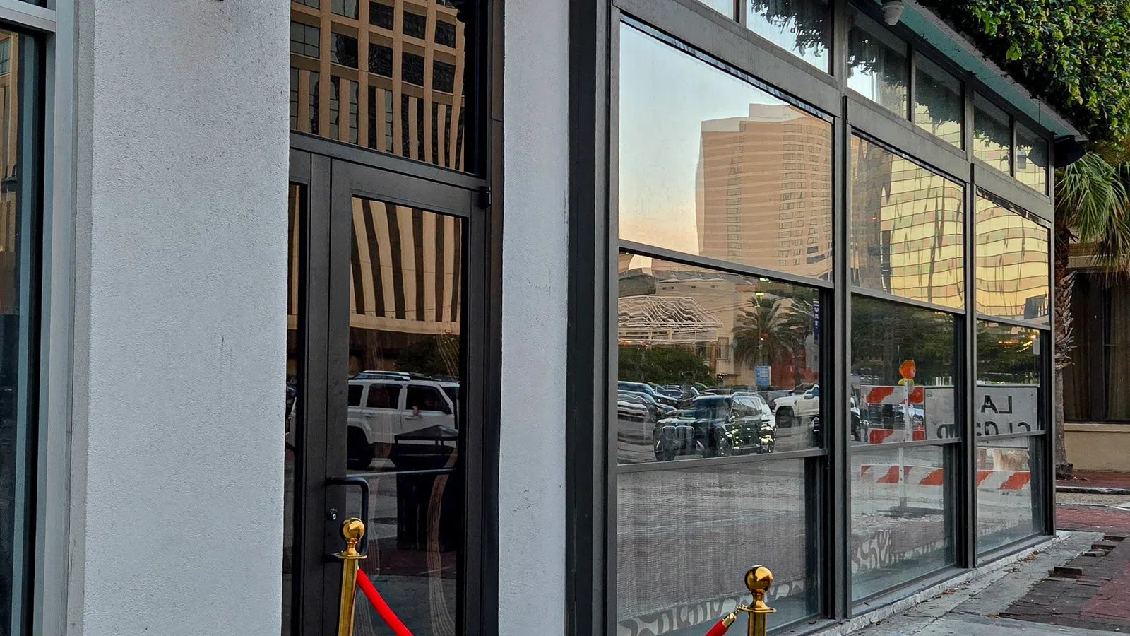 Entrance to KIRA with black door, red velvet rope, gold stanchions, and green ivy on urban building facade.