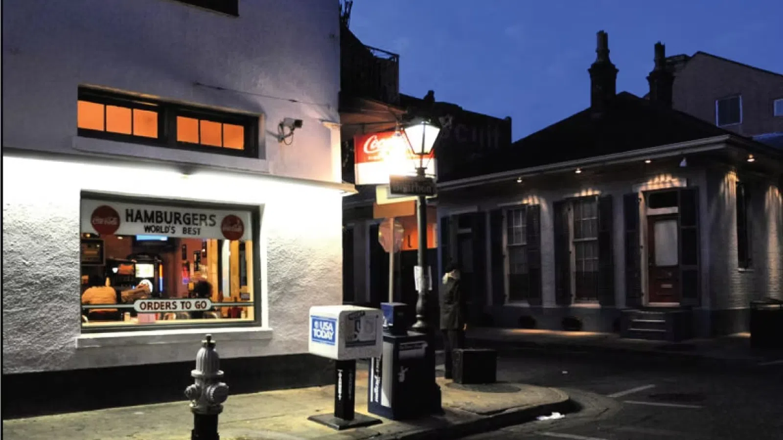 Night street scene with a brightly lit hamburger restaurant window and a nearby streetlamp illuminating the corner.