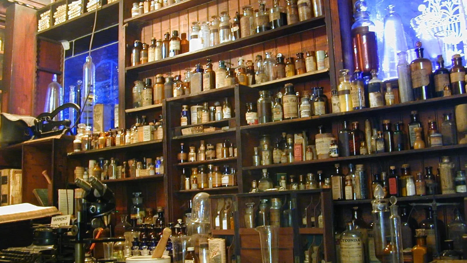 Shelves filled with vintage apothecary jars and bottles in an old-style pharmacy setting.