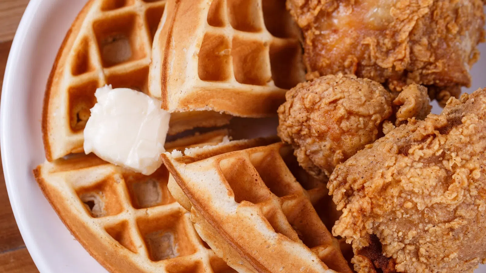 Crispy fried chicken pieces served with golden waffles and a dollop of melting butter on a white plate.