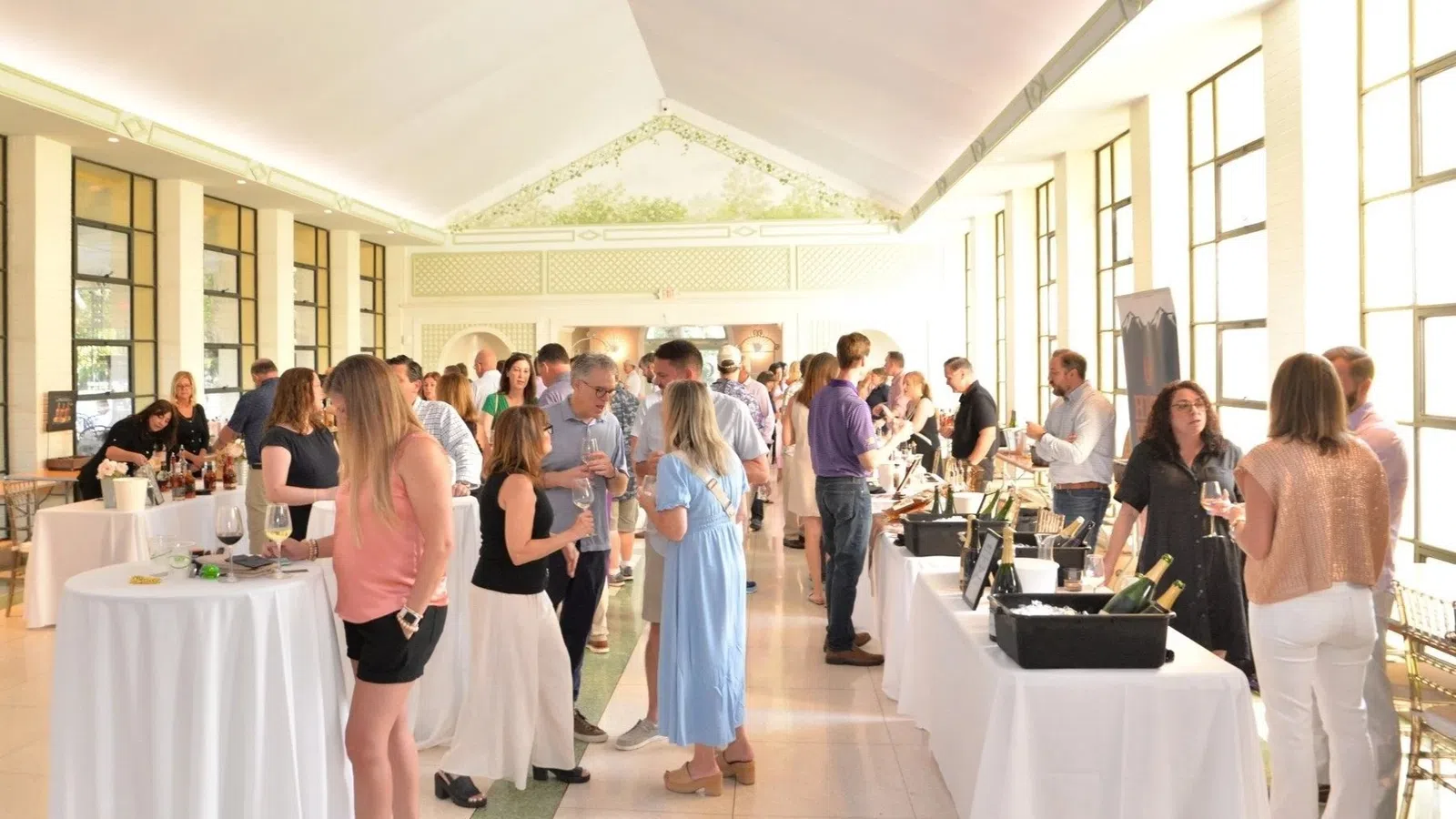Guests mingle and sample wines at an indoor tasting event with bright natural light and elegant decor