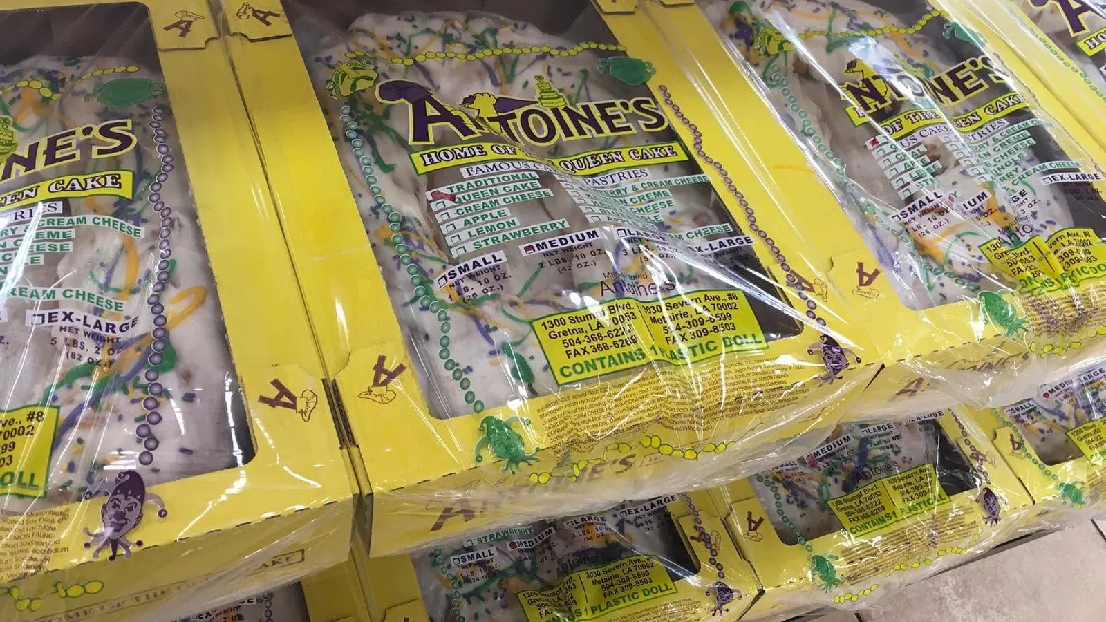 Stacked boxes of Antoine's King Cake with yellow packaging, showcasing traditional Mardi Gras colors and design.