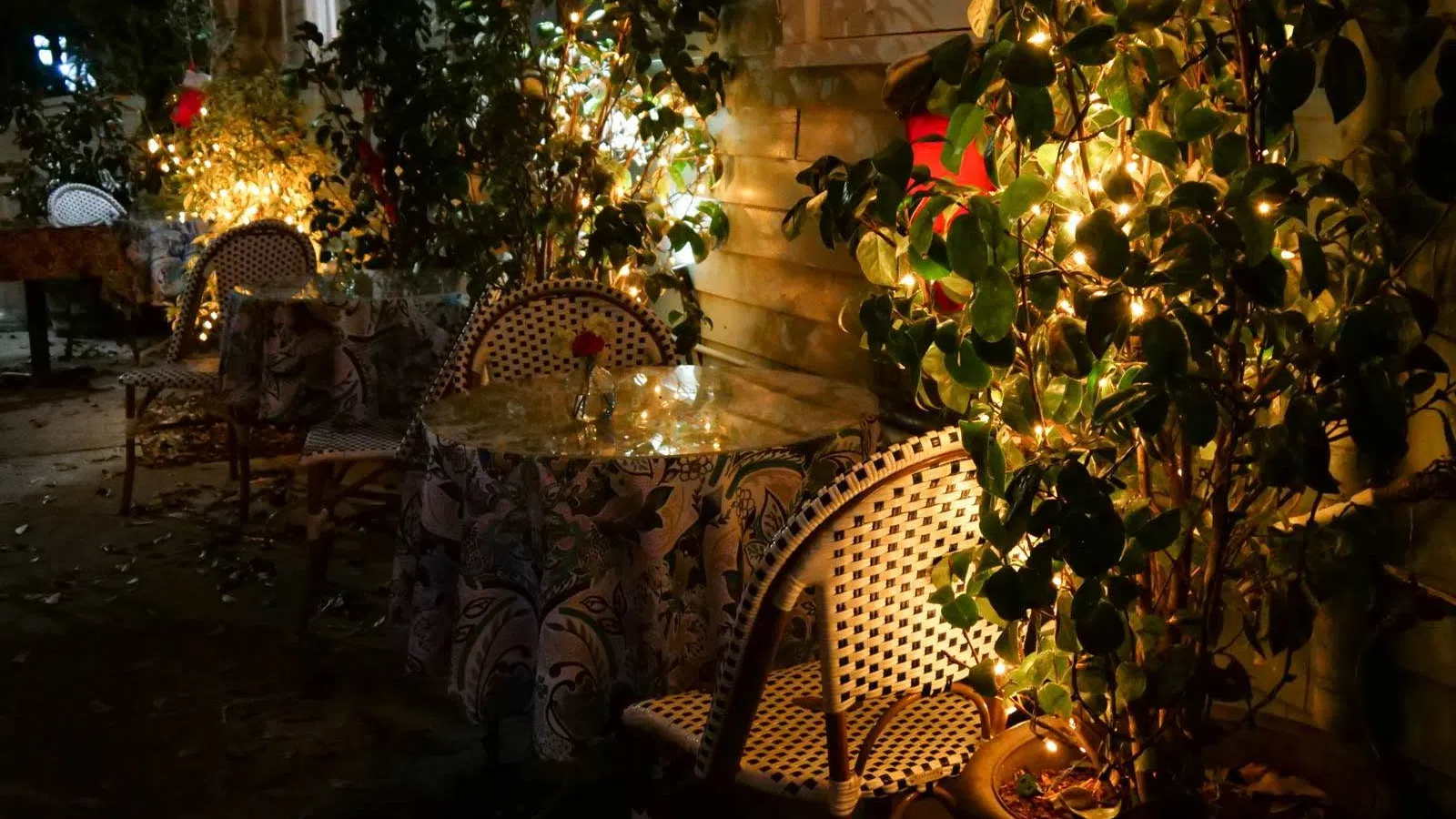 Cozy outdoor cafe seating with patterned chairs and tables lit by warm string lights at night.