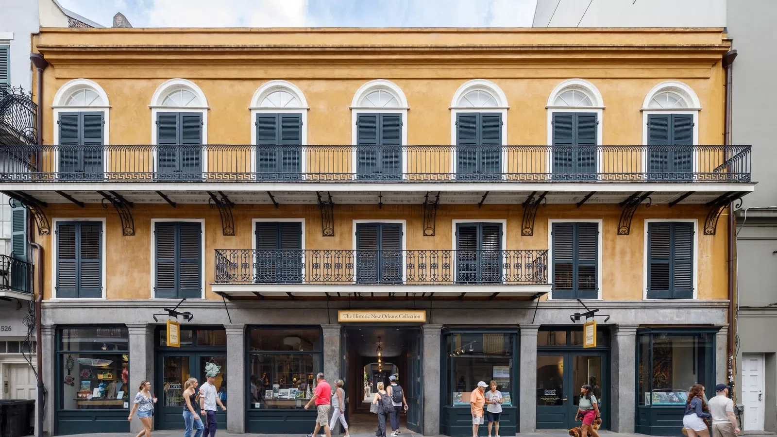 Historic yellow building with black shutters and iron balconies in a lively urban street scene.