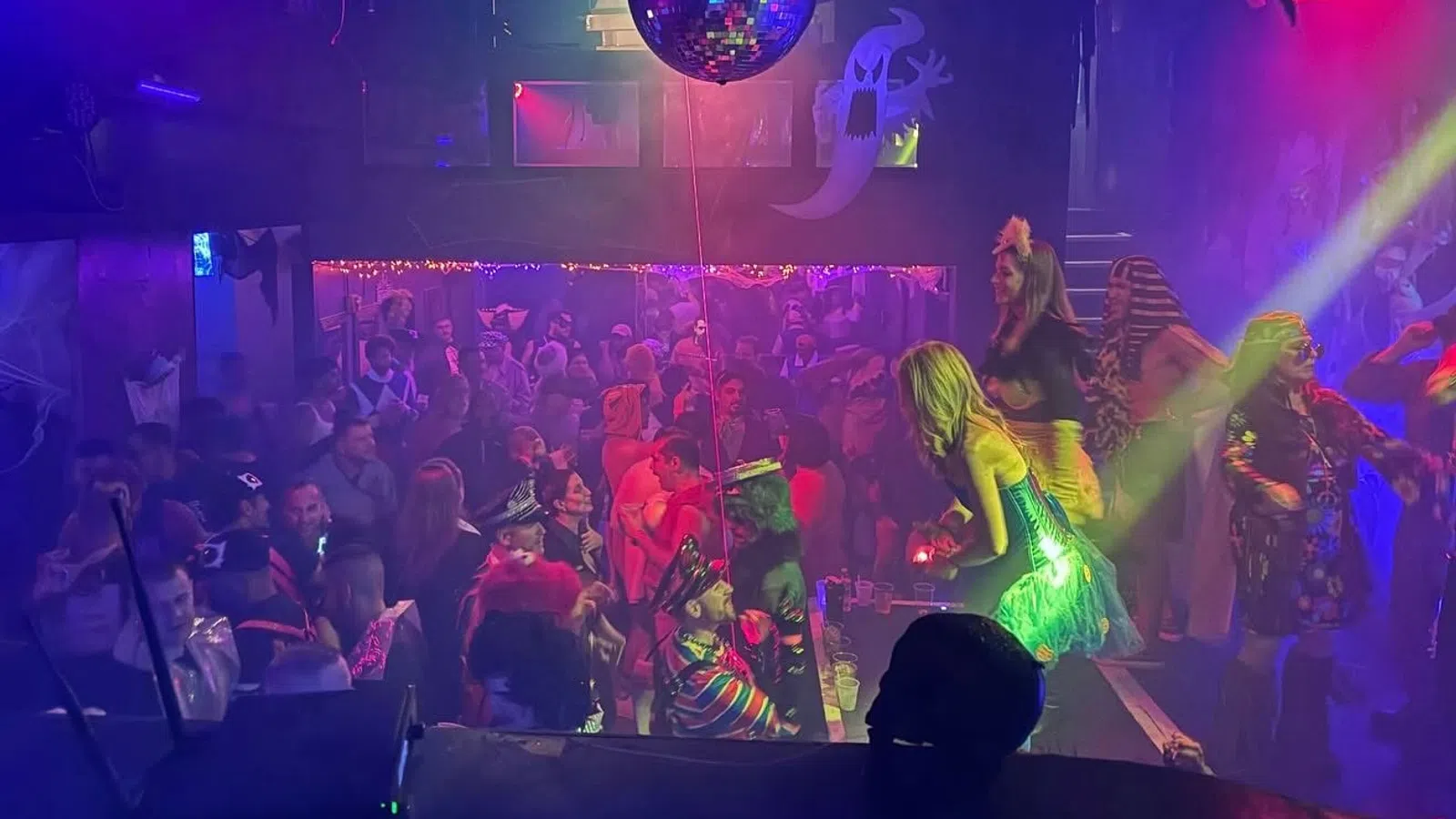 Crowded nightclub with people dancing and colorful lights under a large disco ball during a party