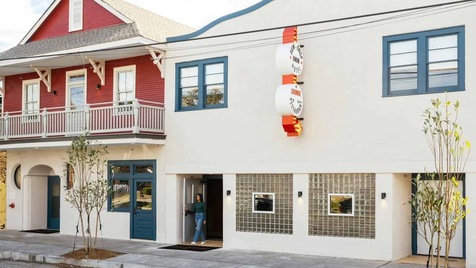 Modern white building with blue accents and a red house with a balcony on the left side in a sunny street.