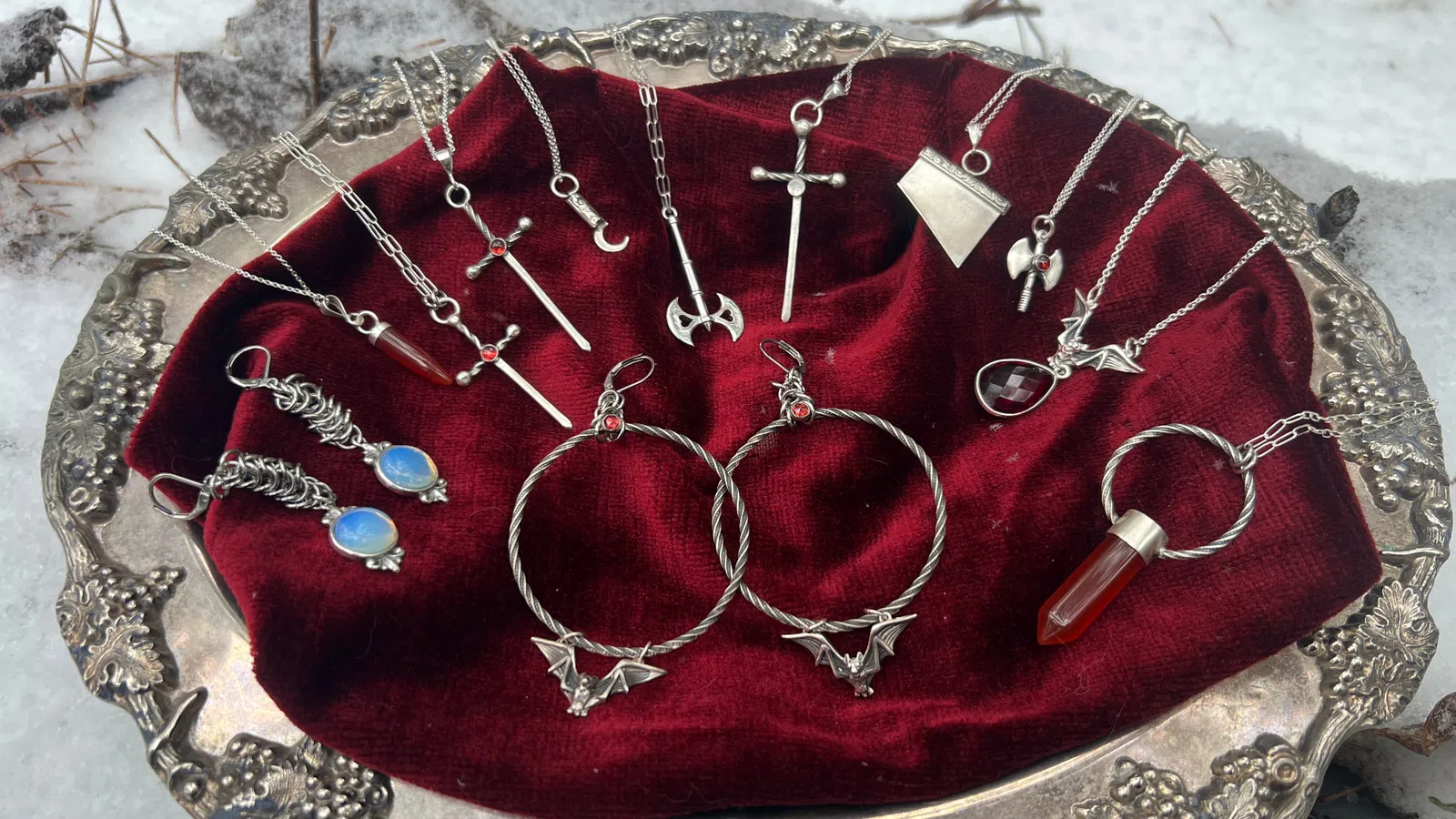 Silver fantasy pendants including swords, crescent moon, dragon, and gemstone jewelry on red velvet in silver tray