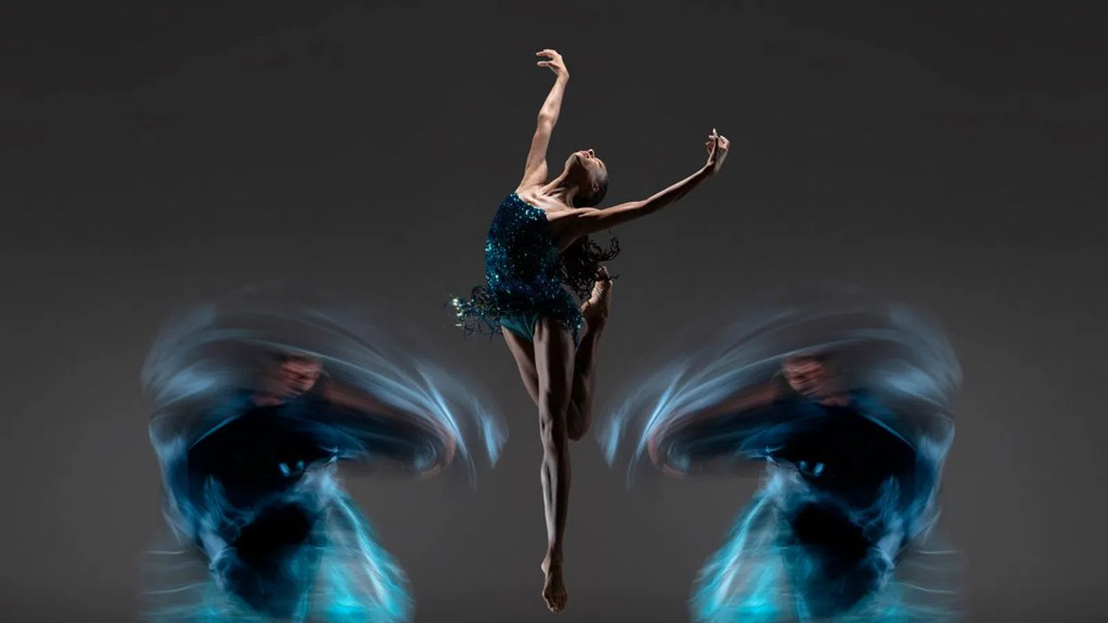 Ballet dancer in mid-air leap with blurred motion trails of dancers spinning on either side against dark background