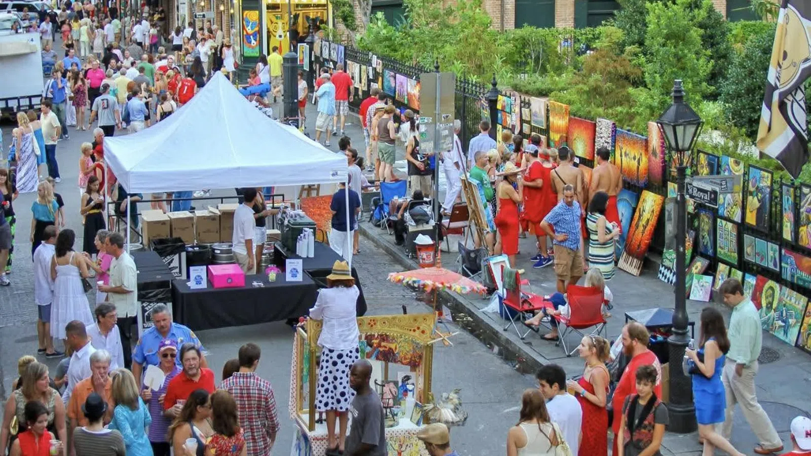 Outdoor art market with crowds browsing vibrant paintings displayed along a street on a sunny day