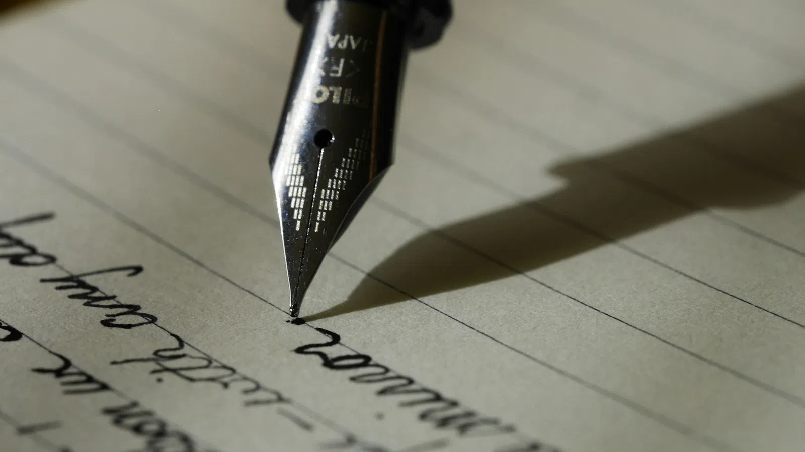Close-up of a fountain pen writing cursive text on lined paper with shadow cast to the side