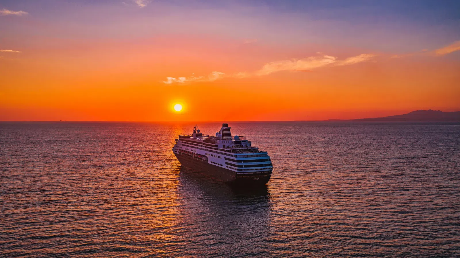 Large cruise ship sailing on calm ocean waters during vibrant orange sunset with clear sky.