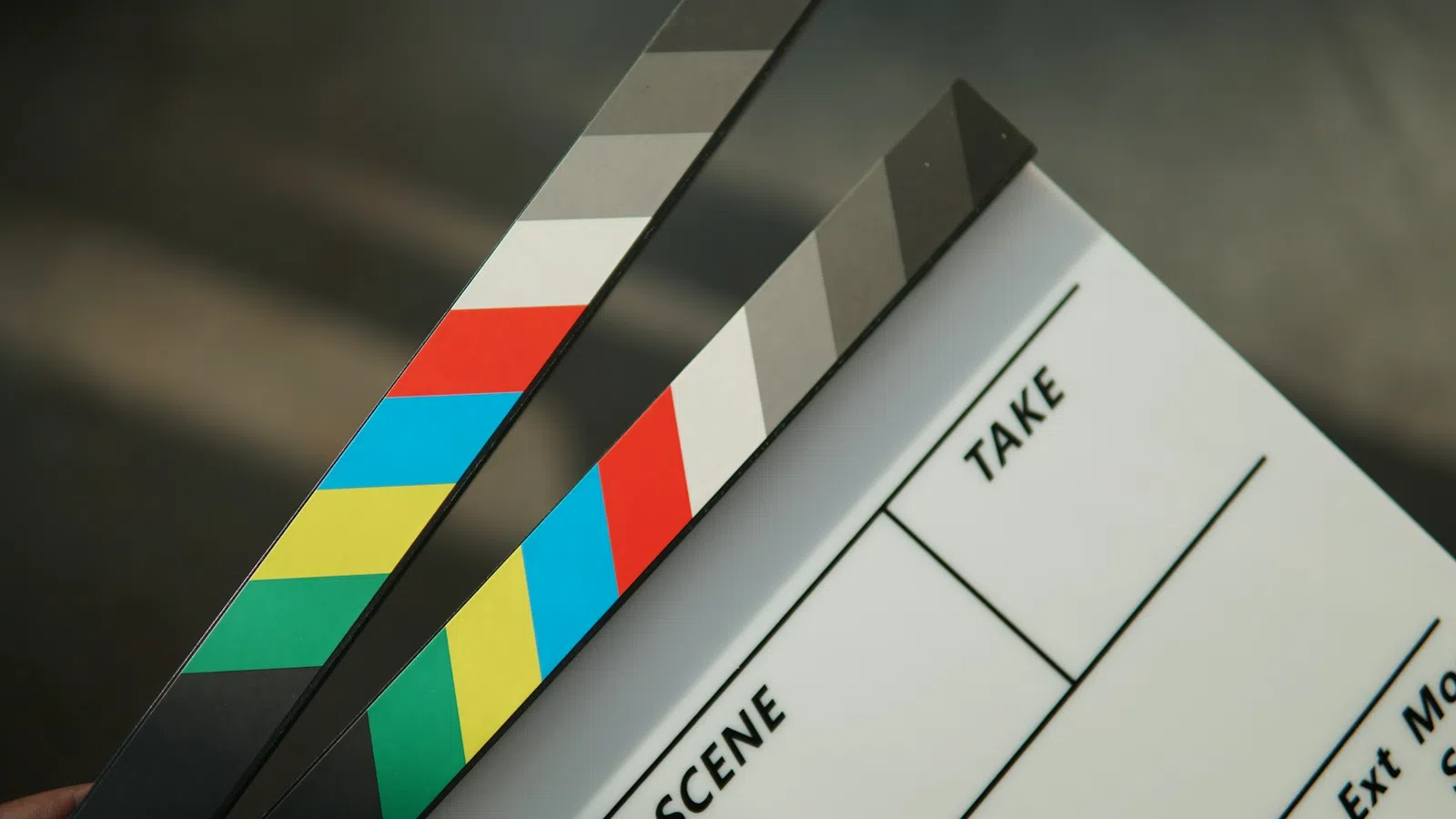 Hand holding a colorful film clapboard with sections for scene and take against blurred background
