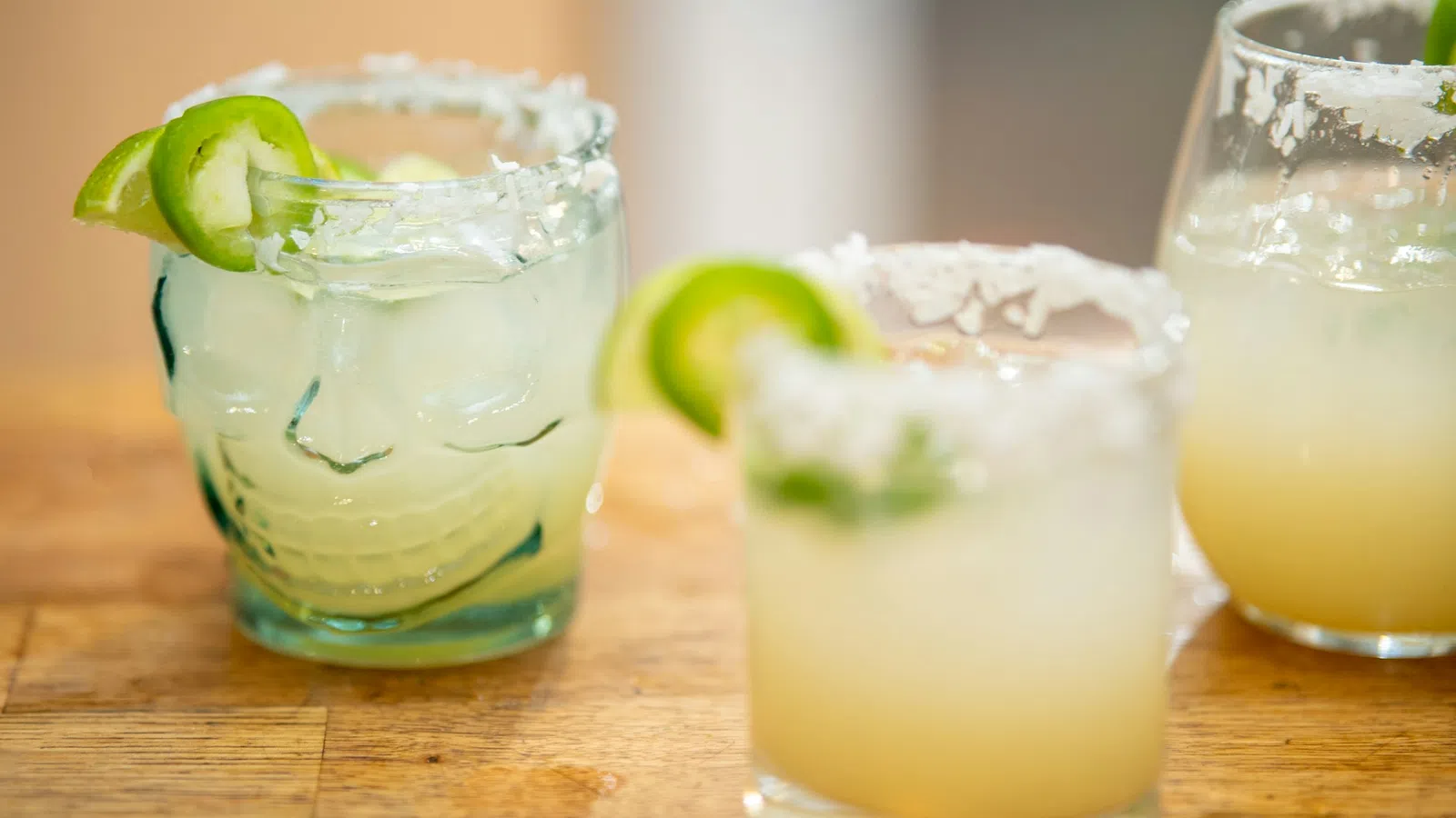 Three margarita cocktails with salted rims and lime garnish on a wooden surface.