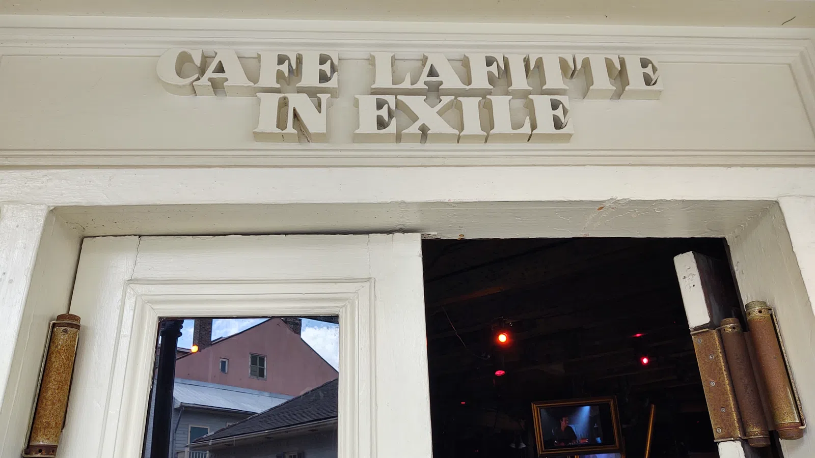 Entrance of Cafe Lafitte in Exile with white wooden doors and reflective glass showing buildings outside.