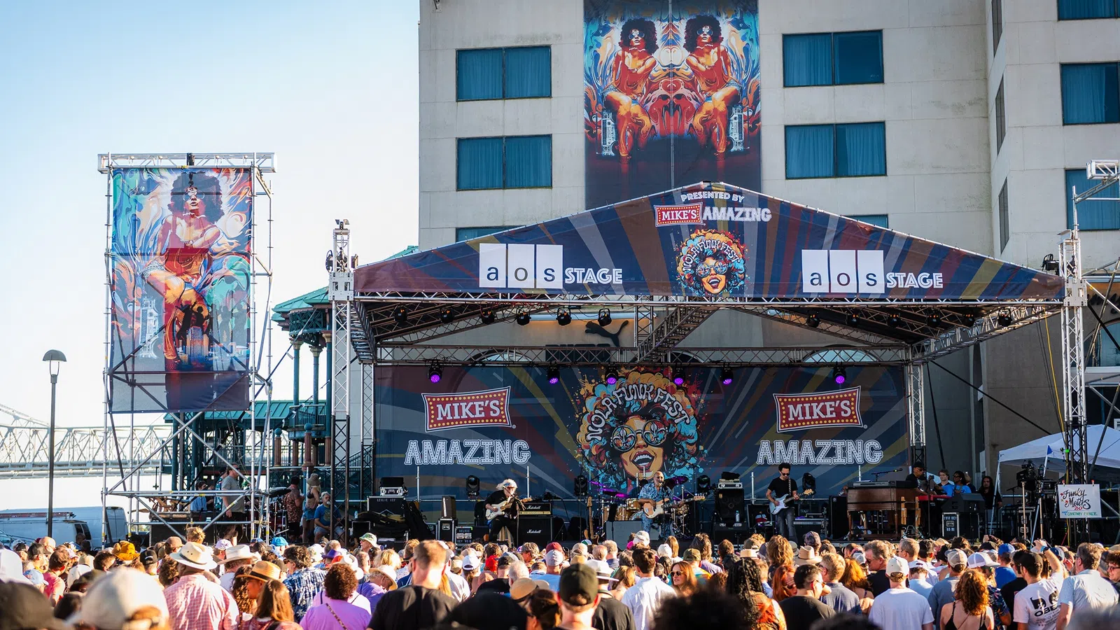 Outdoor music festival on Mike's Amazing stage at Riverwalk with large crowd enjoying live band performance.