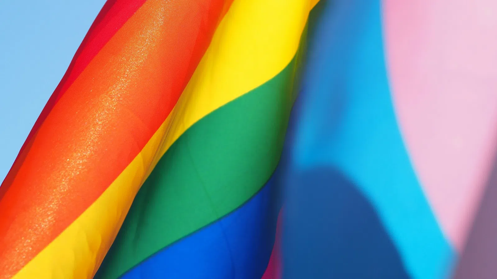 Close-up of a vibrant rainbow pride flag with red, yellow, green, blue, and surrounding colors against a blue sky.