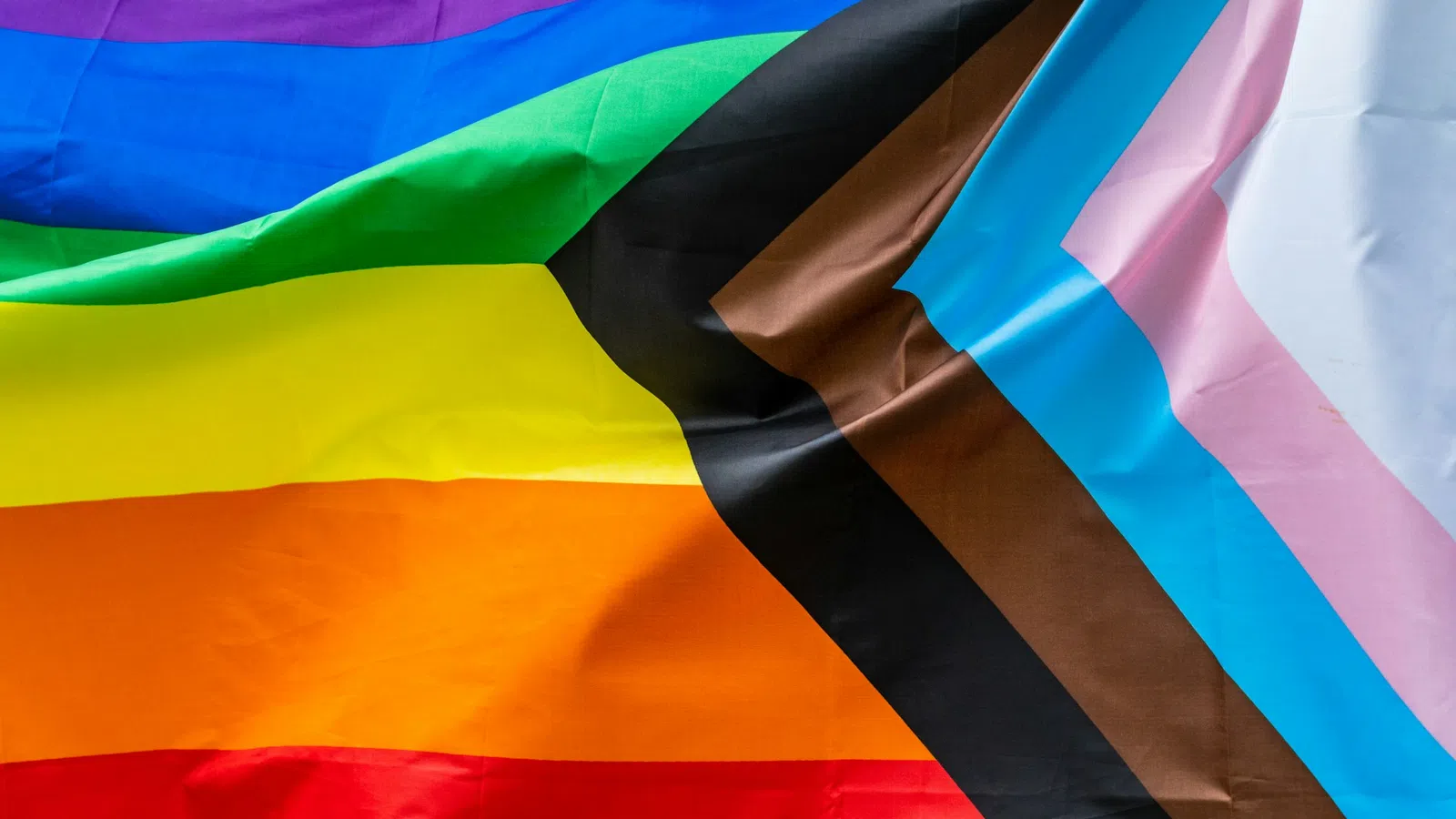 Close-up of the Progress Pride flag showing rainbow, black, brown, and transgender colors with fabric folds.