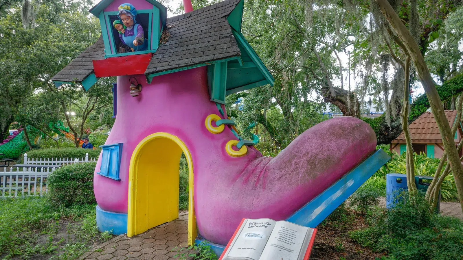 Large whimsical pink boot-shaped playhouse with blue roof and yellow door in a park setting