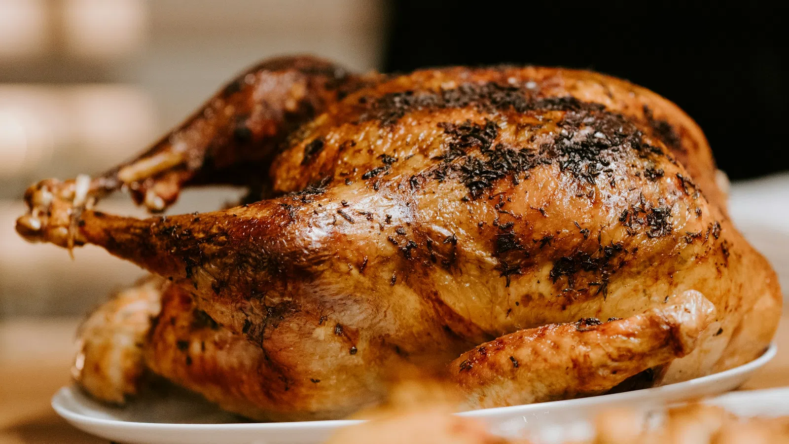 Golden-brown roasted whole chicken with herbs on a white plate ready to serve.