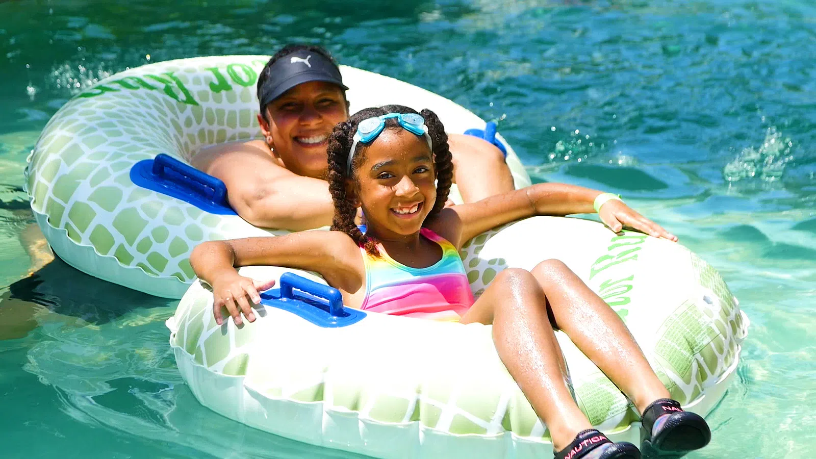 Smiling woman and girl in colorful swimsuit enjoying a sunny day on inflatable tubes in clear water.