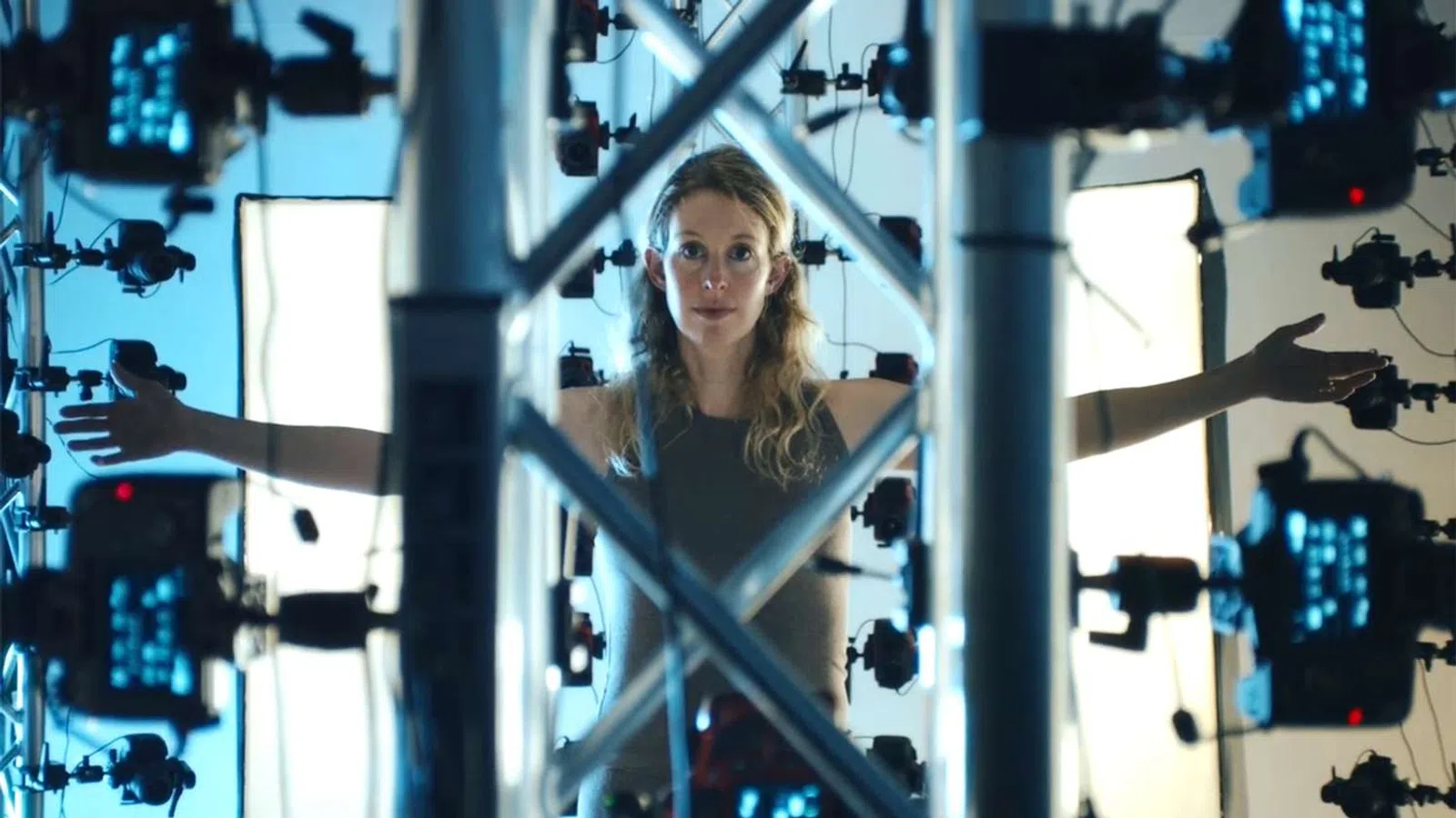 Woman standing inside a 3D scanning rig with arms outstretched surrounded by cameras and lighting panels.