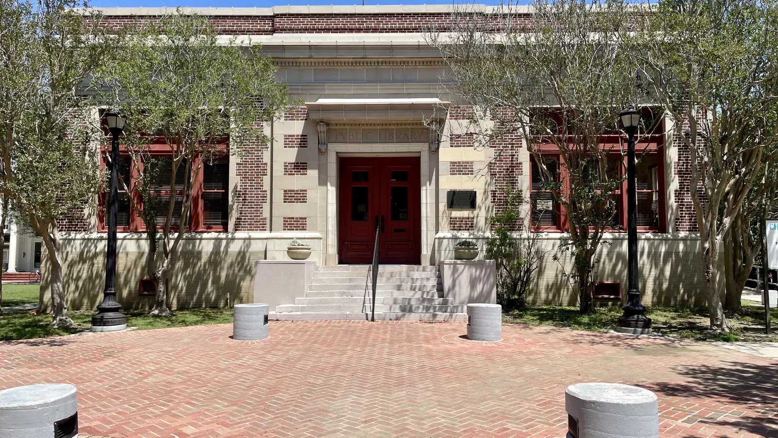 Brick building with red doors and windows, flanked by trees and black street lamps under a clear blue sky.