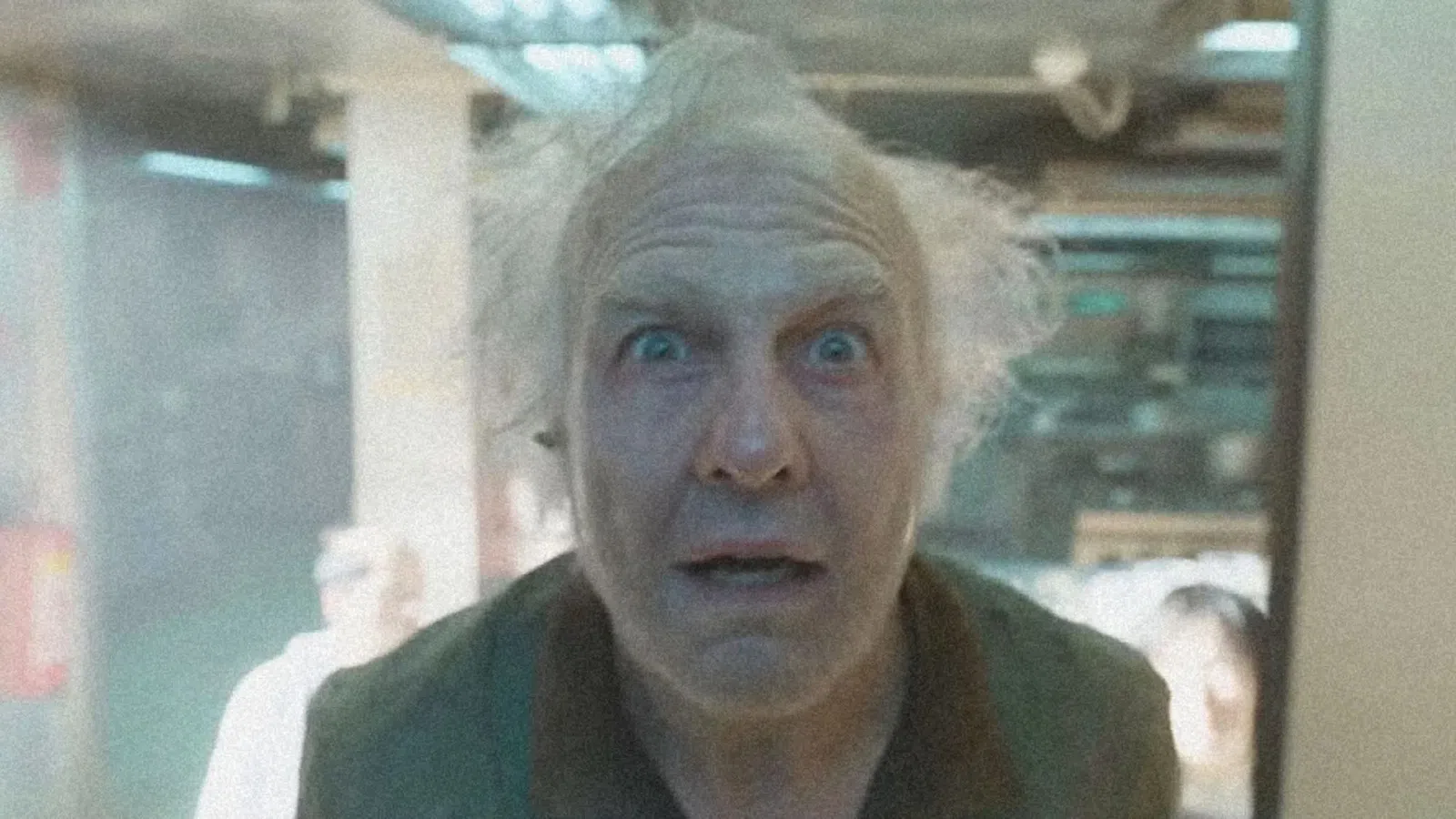 Older man with wild white hair and surprised expression looking directly at the camera indoors.