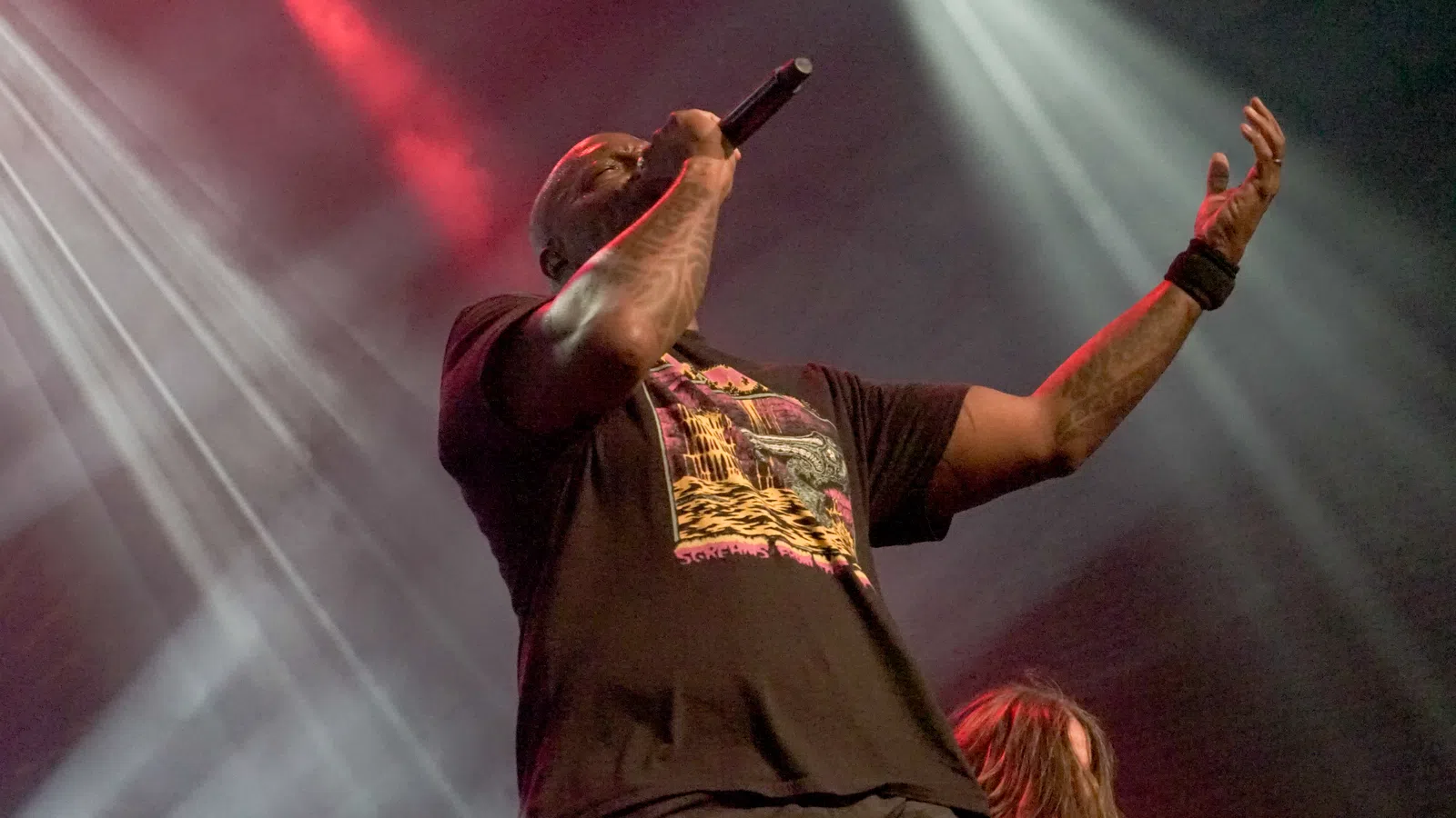 Male rapper performing passionately on stage with microphone amid dynamic stage lighting effects.