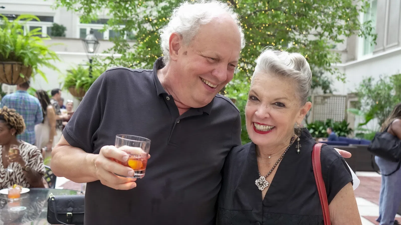 Happy elderly couple enjoying drinks at an outdoor social gathering on a sunny day.