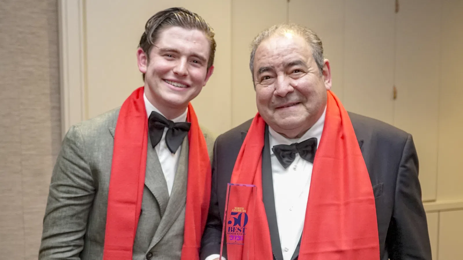 Two men in formal wear with red scarves, one holding a Best Chef award at an event.