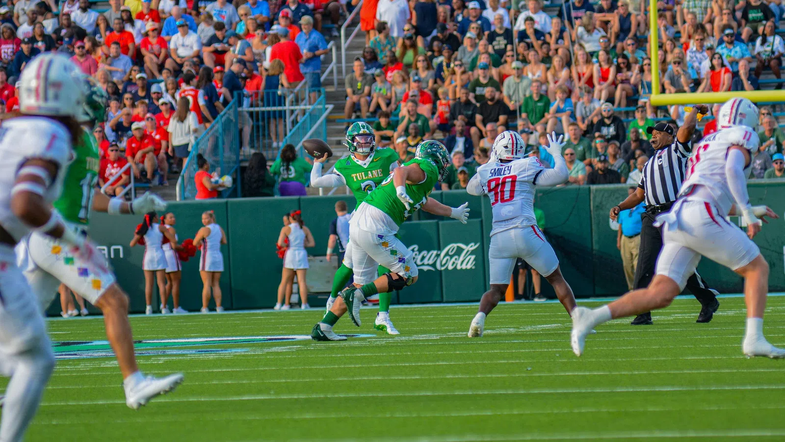 Tulane quarterback prepares to throw under pressure from defenders with crowd and cheerleaders in background