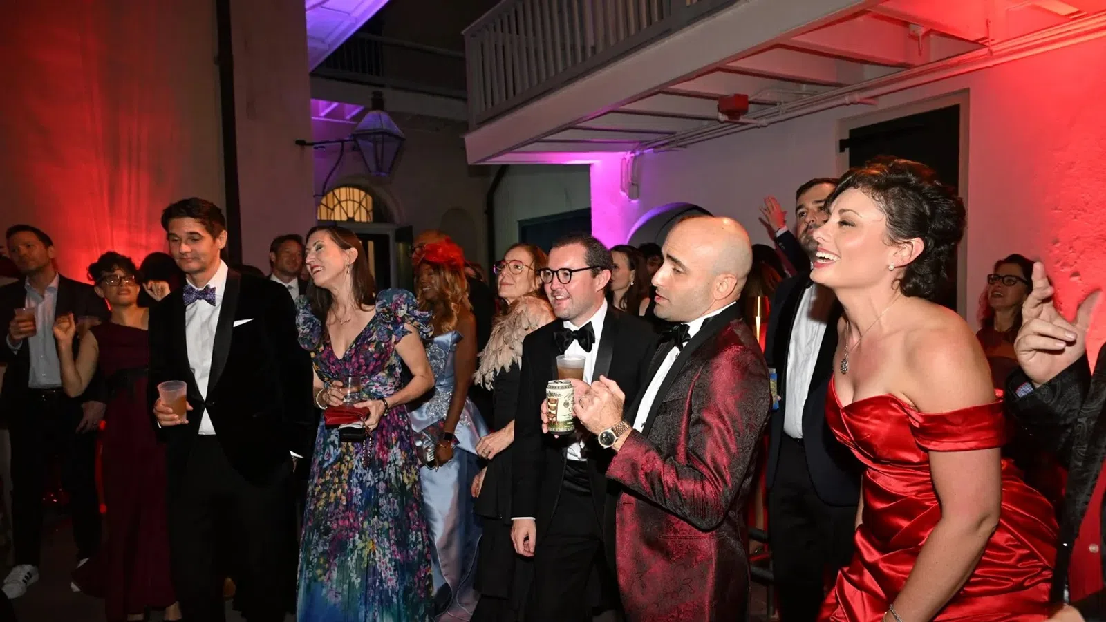 Guests dressed in formal attire enjoy a lively evening party with colorful lighting in an elegant indoor venue.
