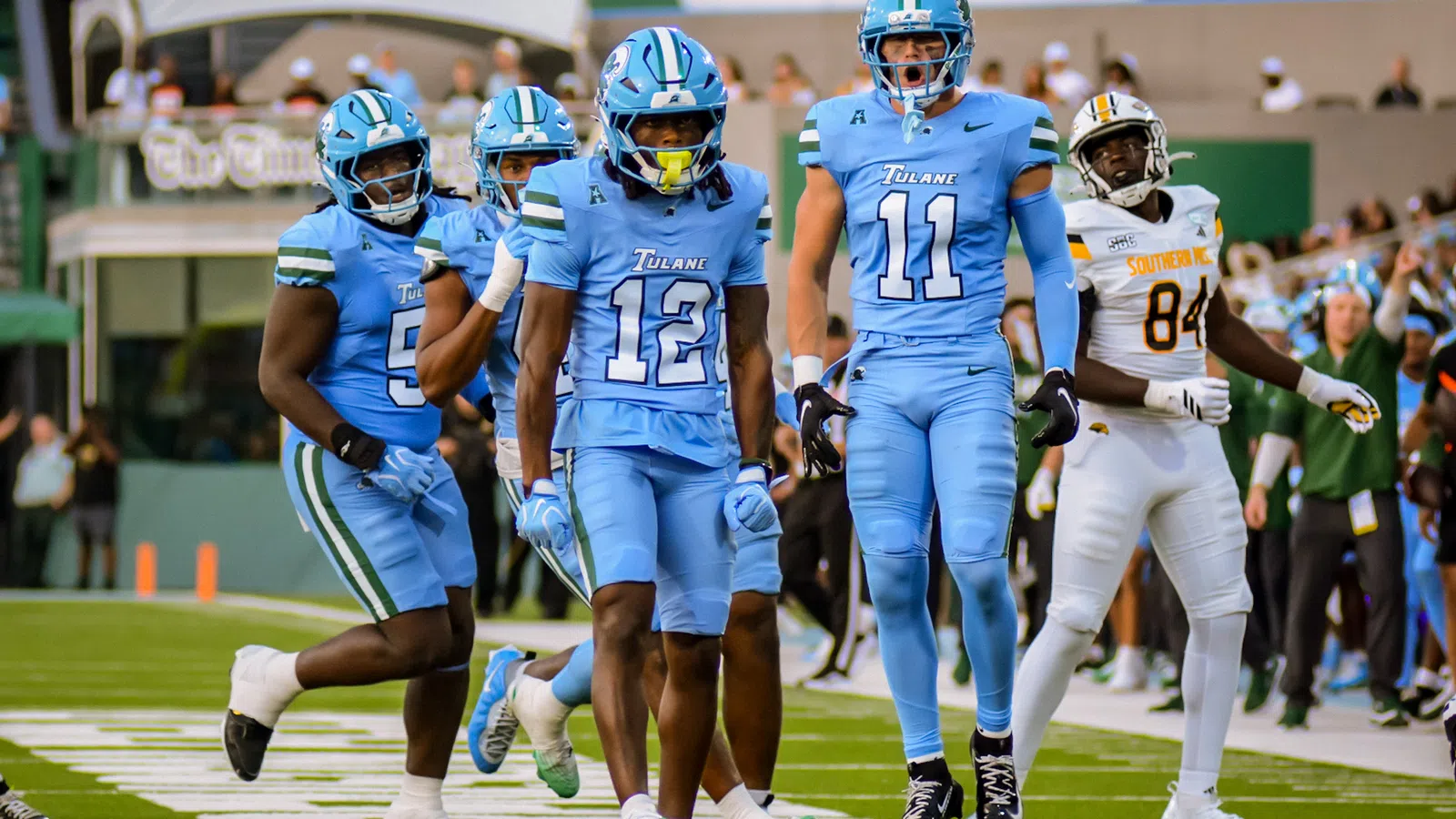 Tulane football players in blue uniforms celebrating on the field during a game against Southern University.