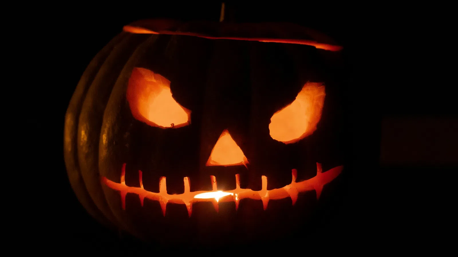 Glowing Halloween jack-o'-lantern with menacing eyes and stitched mouth carved in pumpkin in darkness