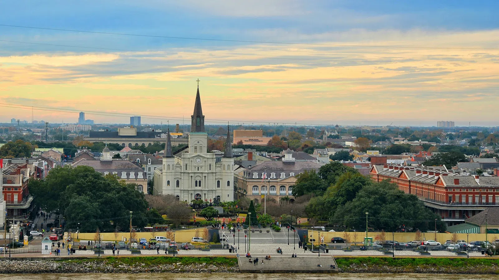 Stunning view of St. Louis Cathedral and Jackson Square with the Mississippi River in the foreground at sunset.