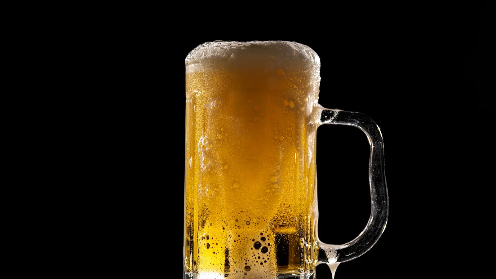 Cold beer mug filled with golden lager and frothy foam against a black background