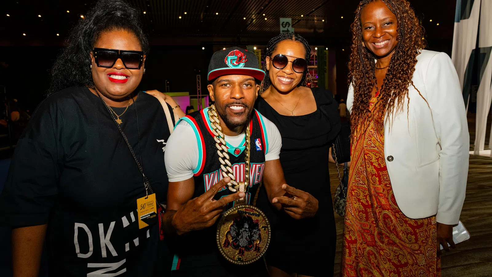 Group of four diverse people smiling at a social event with colorful lighting and casual attire.