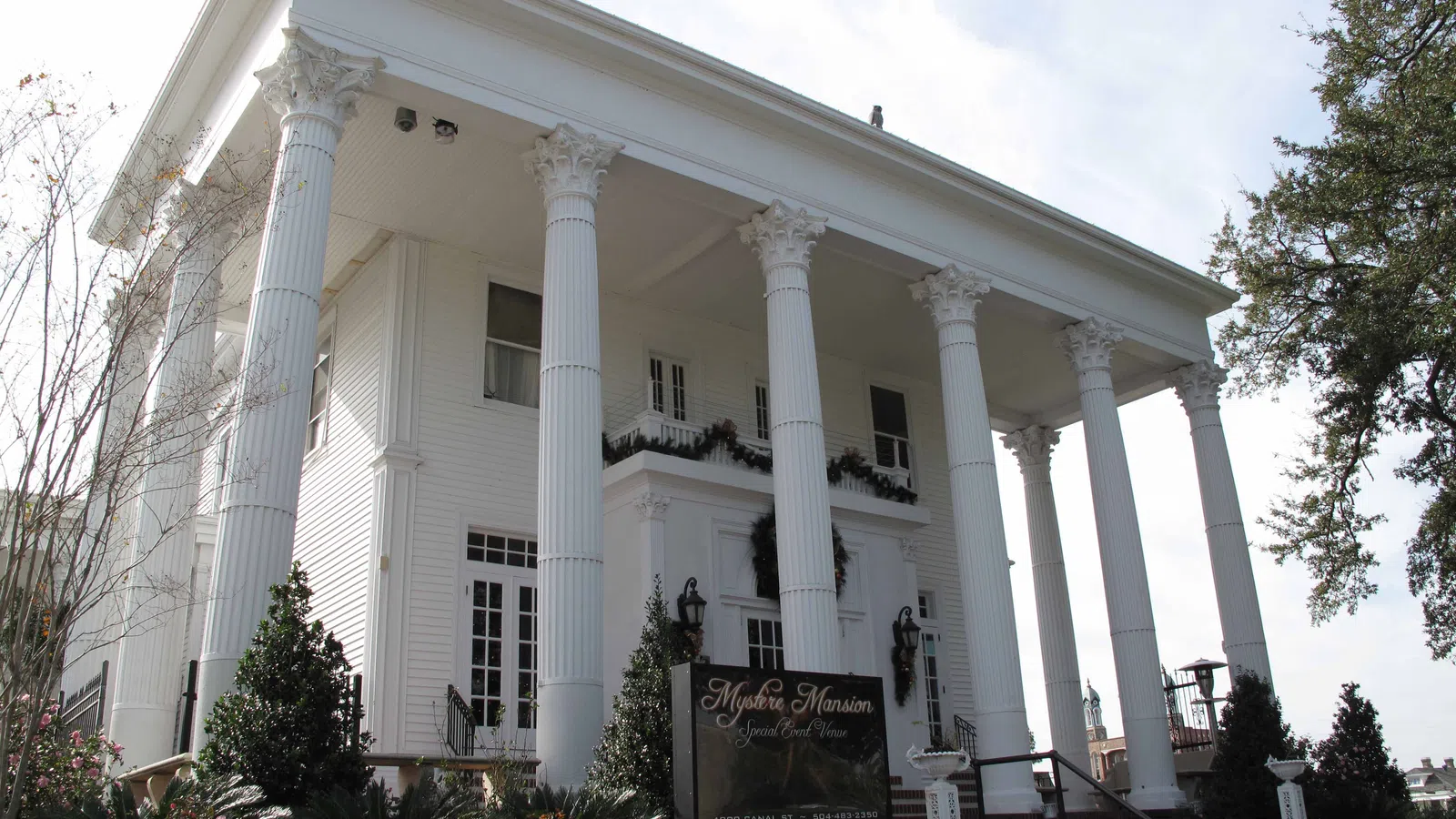 White Greek Revival mansion with tall Corinthian columns and manicured garden in front under a clear sky.