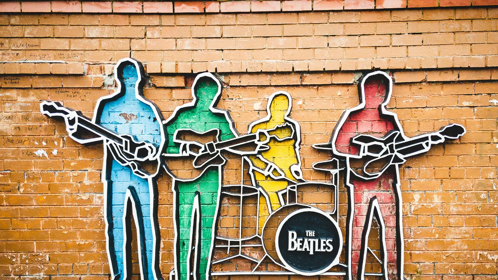 Colorful Beatles band silhouettes mural on brick wall with instruments and drum featuring their band name.