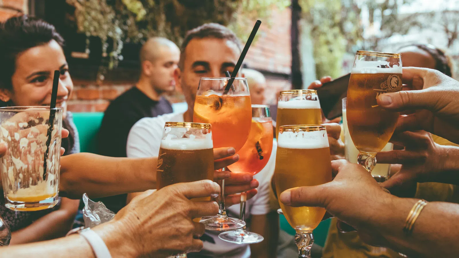 Group of friends clinking glasses with beer and cocktails at an outdoor social gathering.
