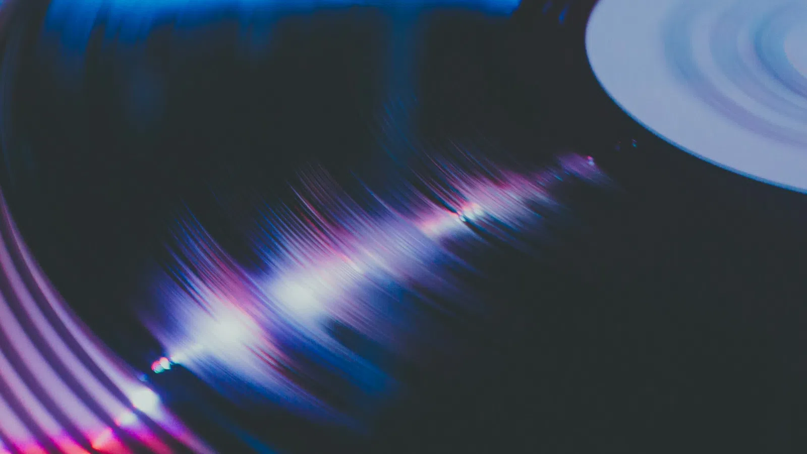 Close-up of a vinyl record spinning with colorful light reflections on its grooves in a dark setting