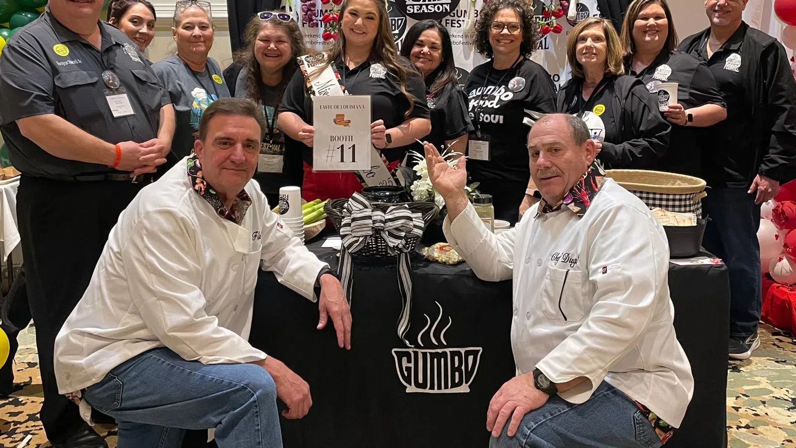 Group of people posing at Gumbo Season Fest booth with festive decorations and promotional materials.